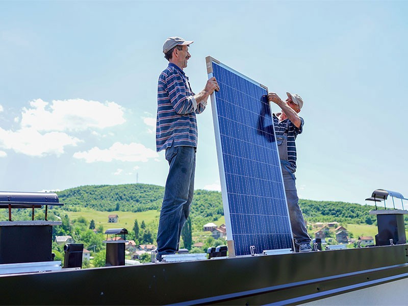 Two middle aged man setting up a solar panel on roof